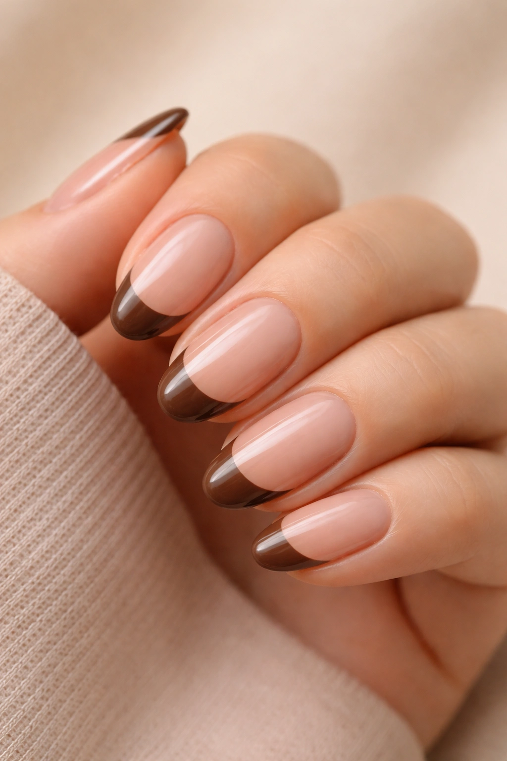 Close-up of short almond nails with sheer brown French tips on a neutral backdrop