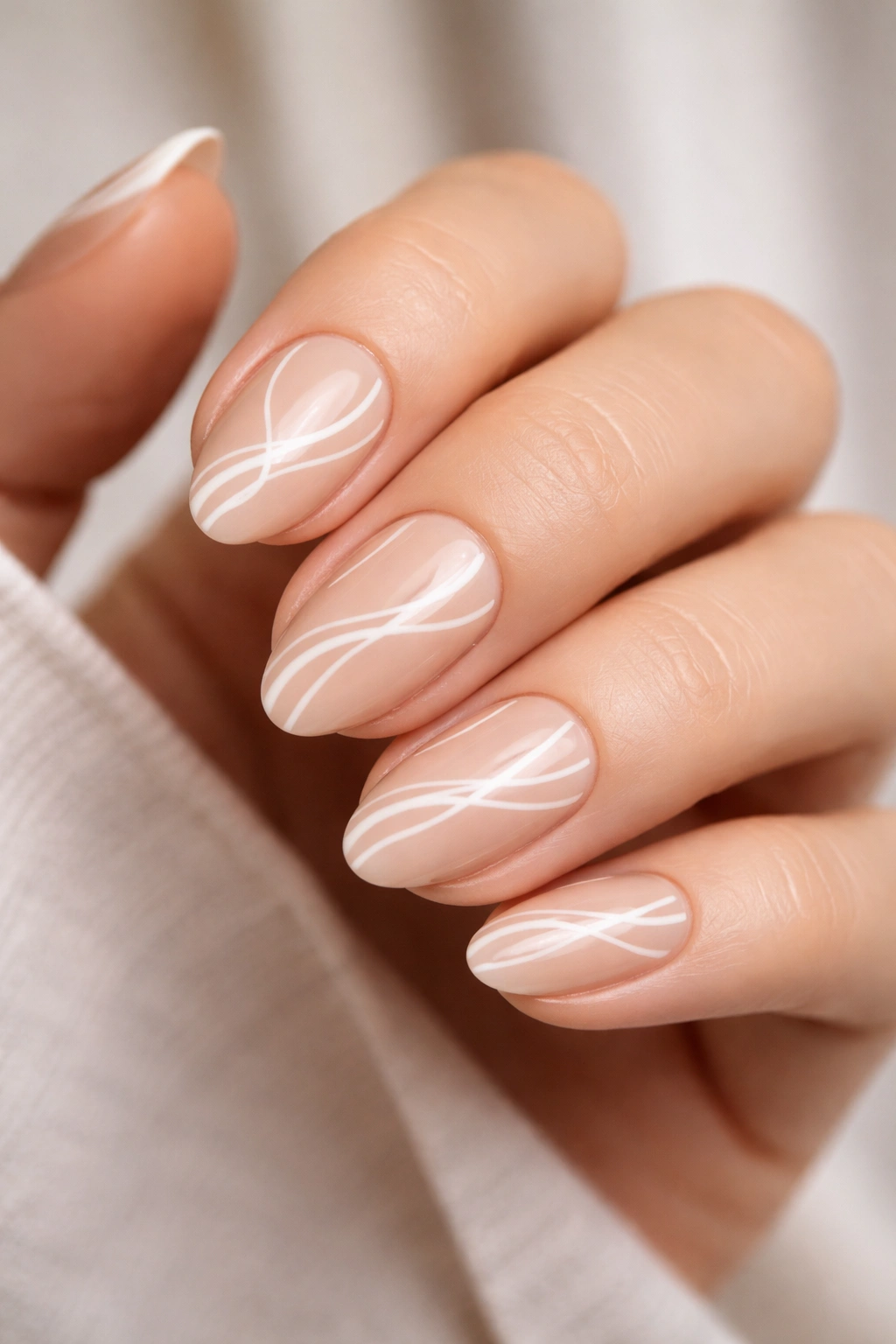 Close-up of short almond nails with sheer nude base and white ribbon swirl nail art