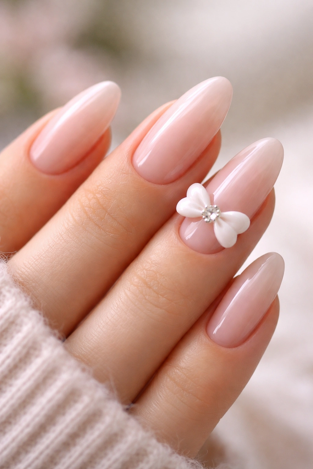 Sheer pink long oval nails with a tiny 3D bow on one nail