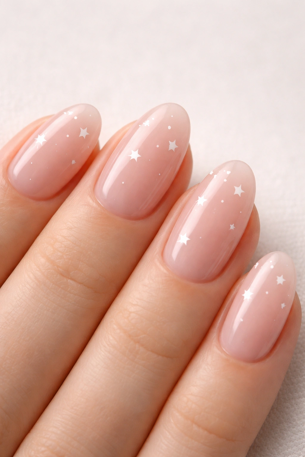 Close-up of sheer pink almond nails with tiny white stars on a neutral surface
