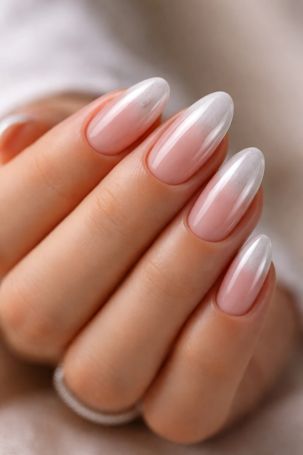 Short almond nails with sheer pink to white chrome ombre on a neutral background