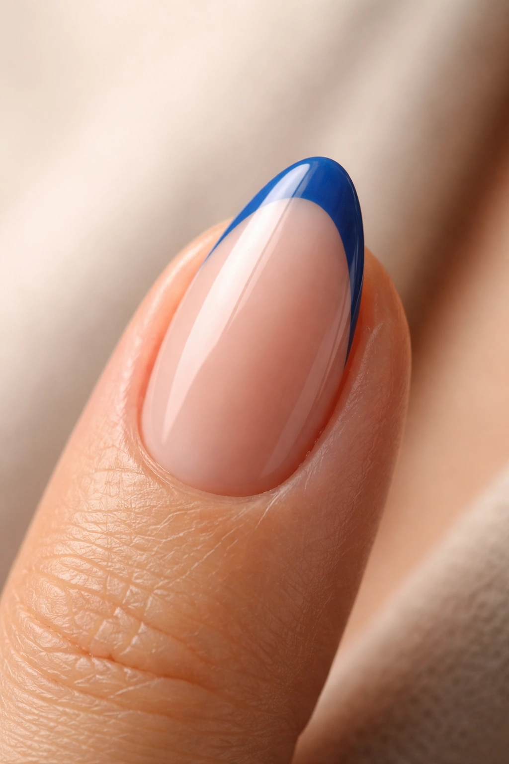 Close-up of a short almond nail with blue French tip on nude base
