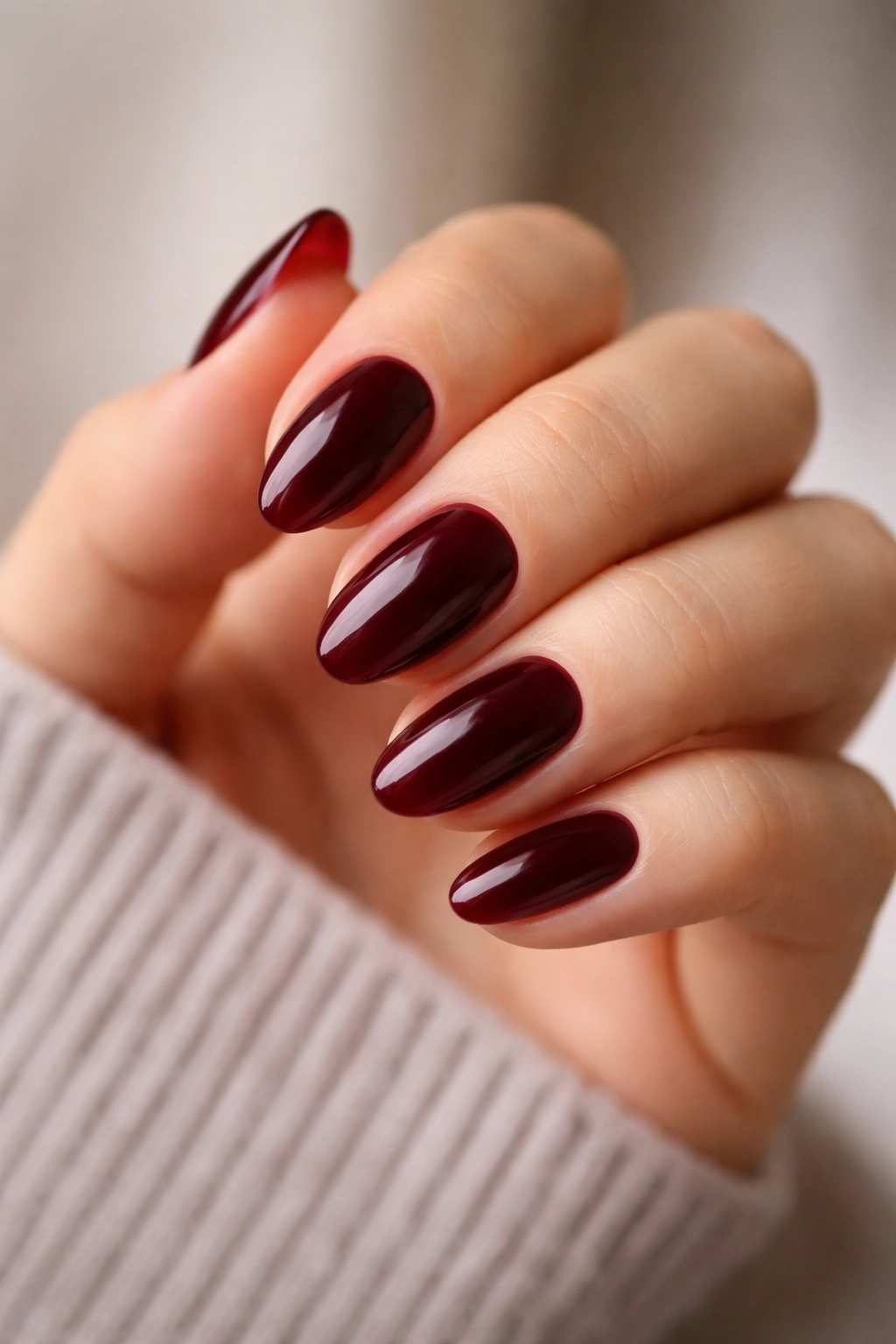 Close-up of short almond nails painted in dark red with a glossy finish
