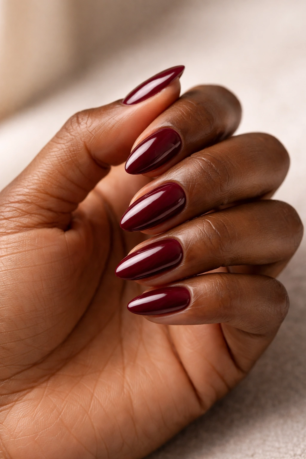 Close-up of dark skin hand with burgundy short almond nails