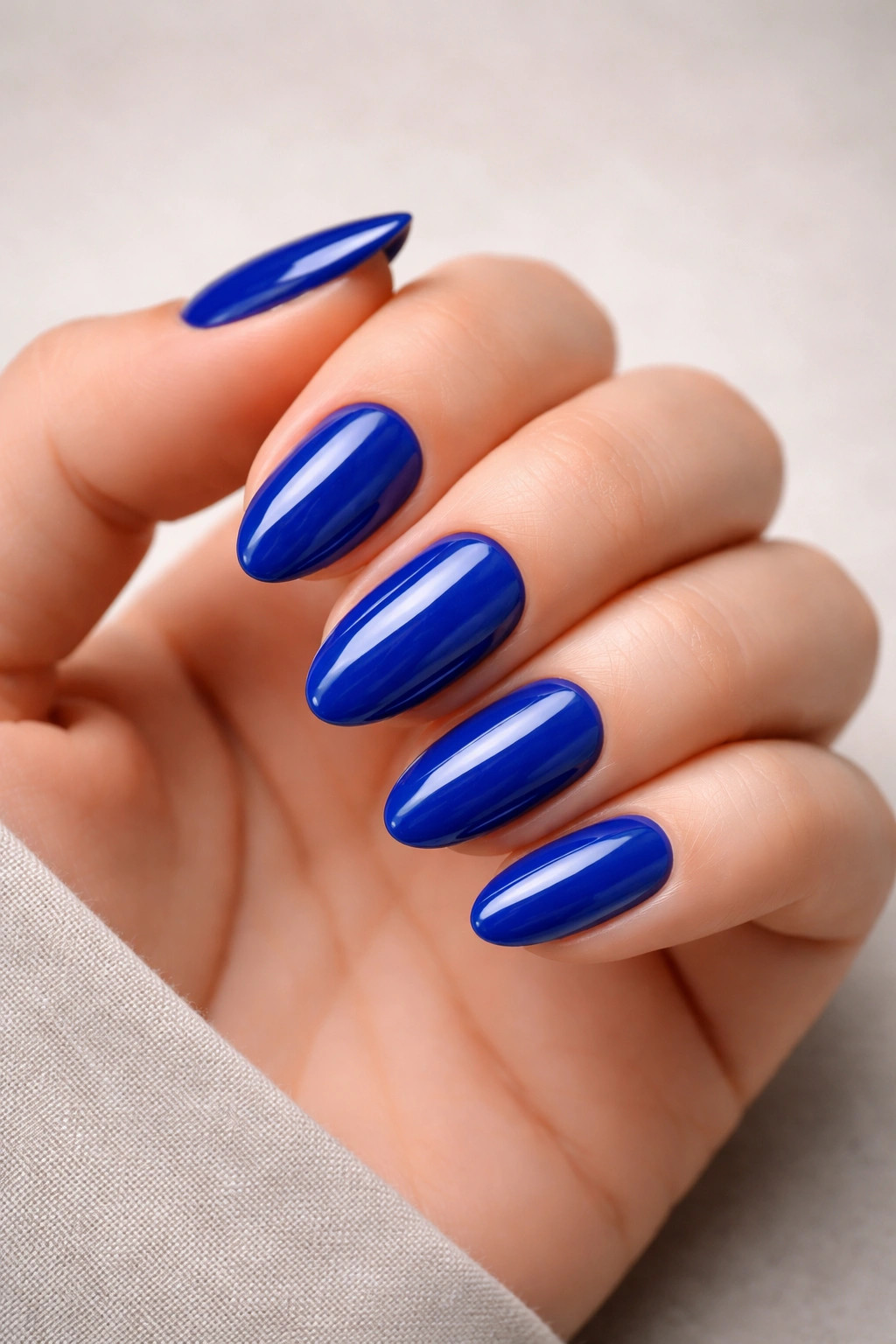 Close-up of glossy royal-blue short almond nails on a hand with a clean studio background