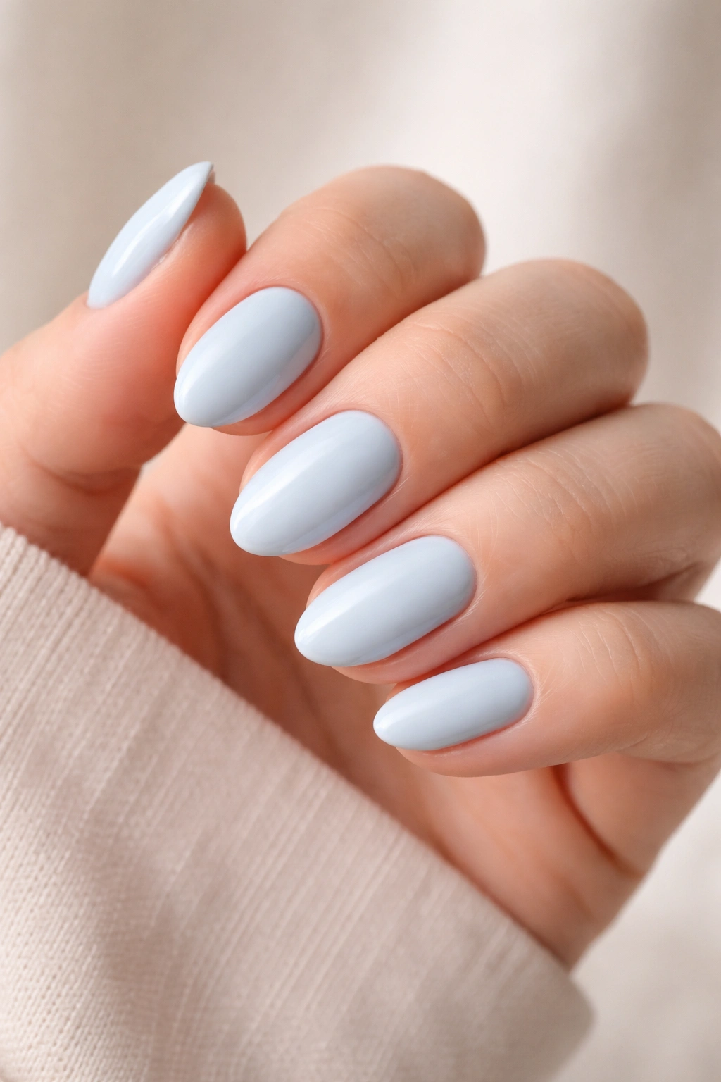 Close-up of short almond nails painted pale blue on a neutral background
