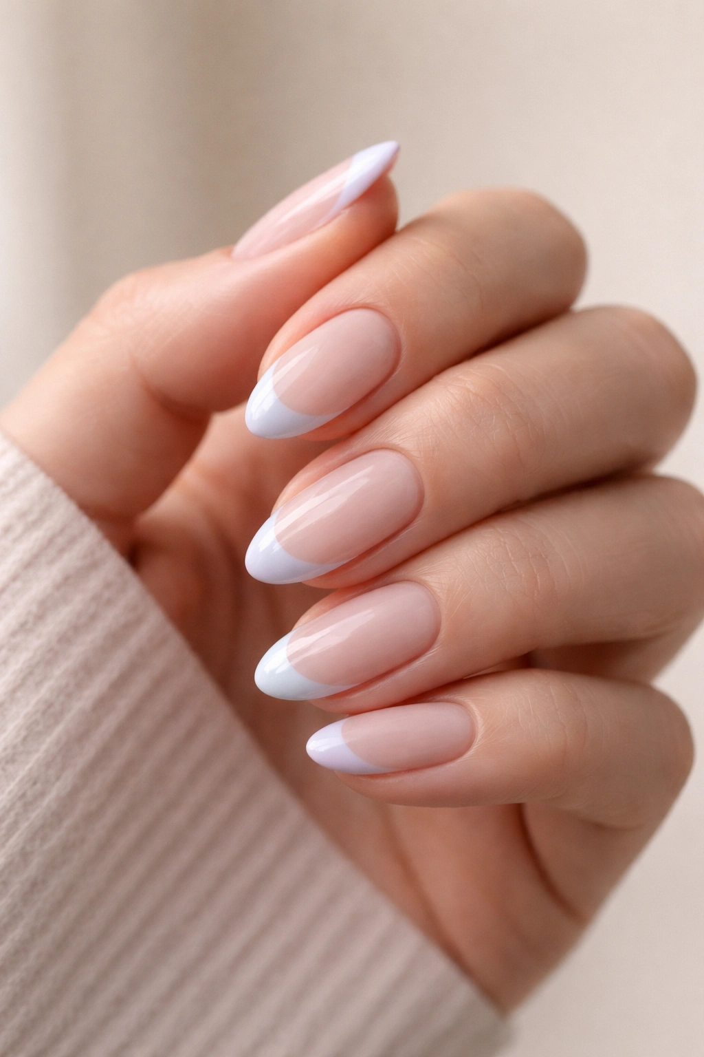 Close-up of short almond nails with pastel French tips on a neutral background