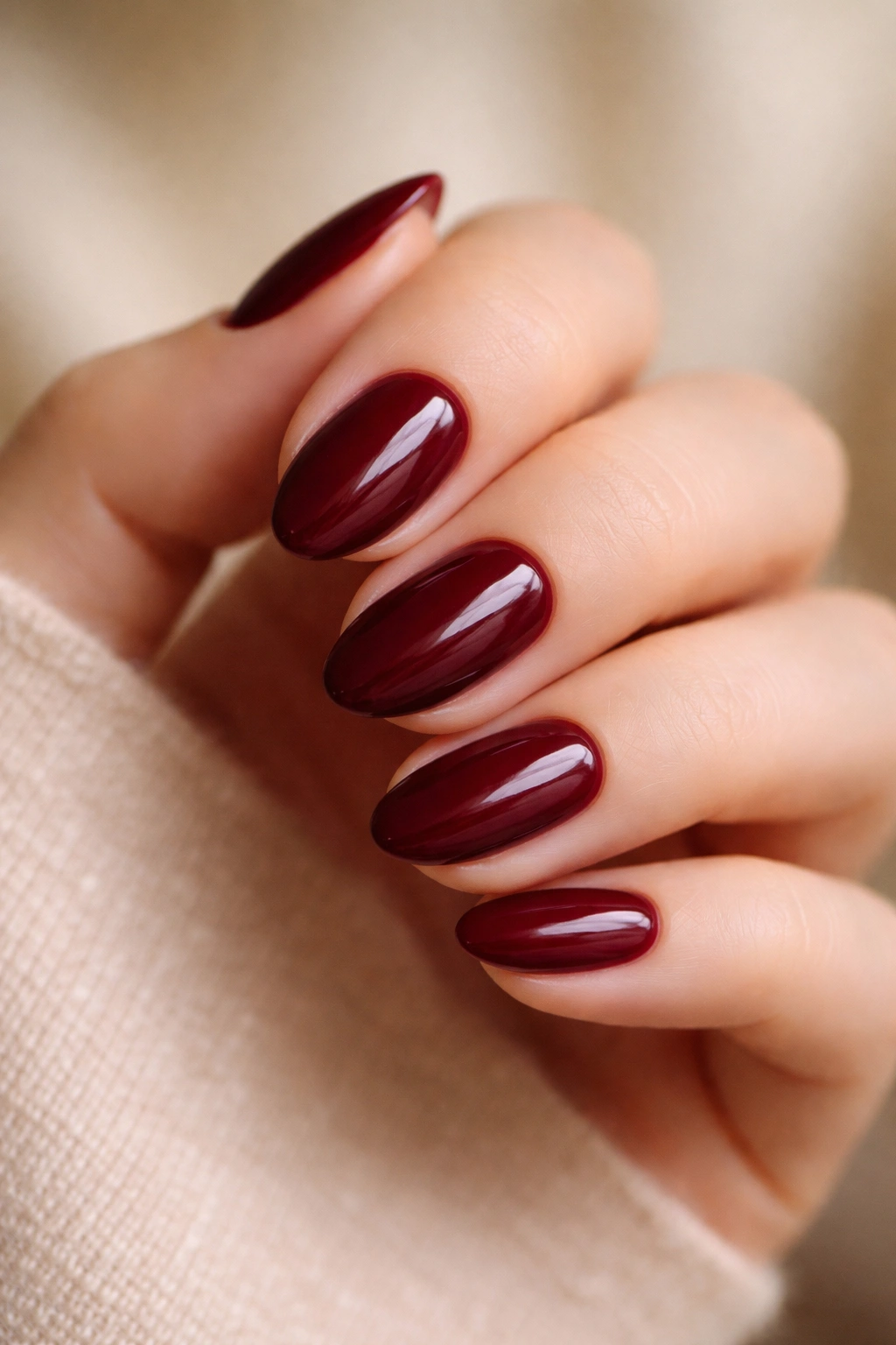 Close-up of short almond nails painted deep wine red highlighting tapered shape