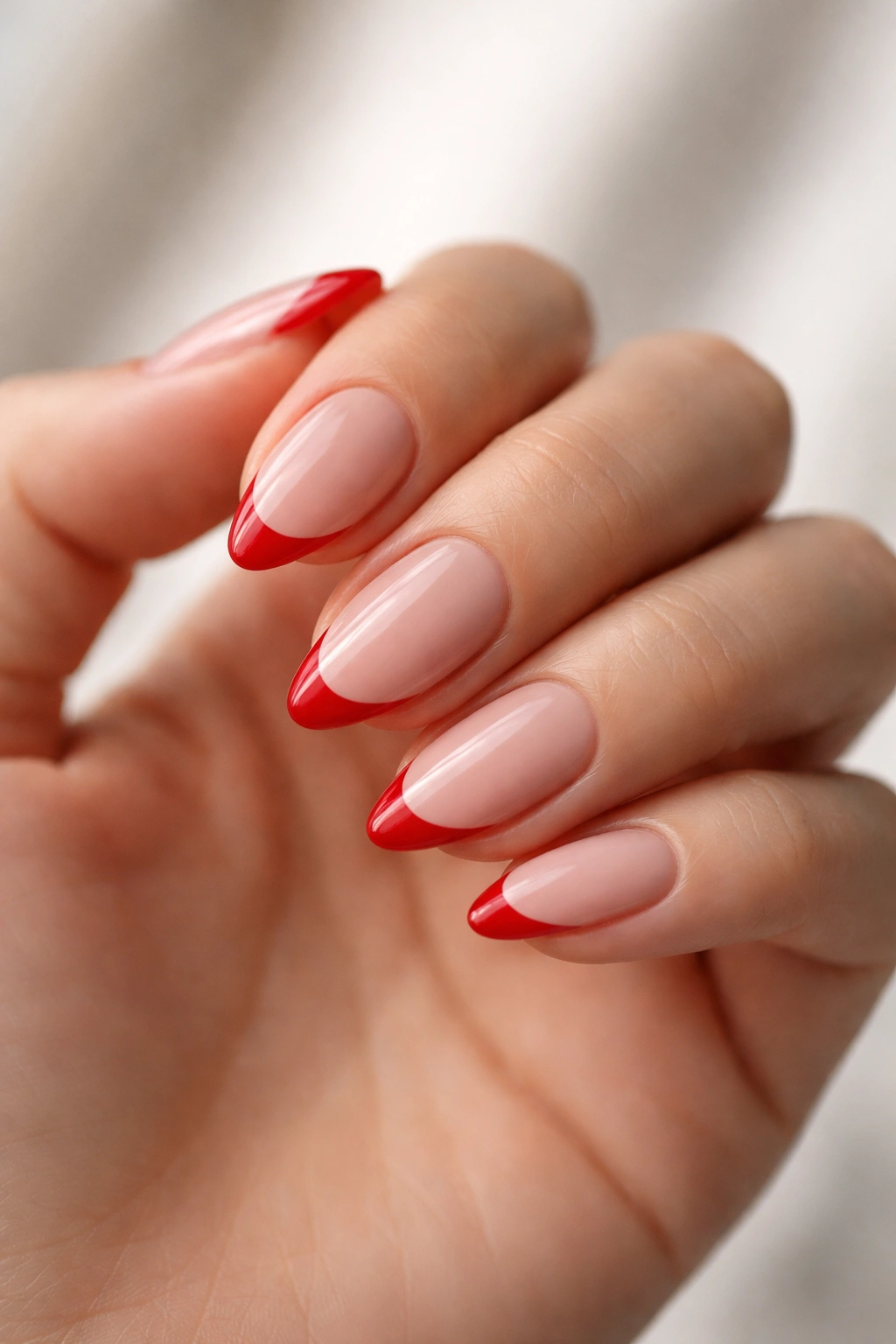 Close-up of short almond nails with red French tips on a nude base