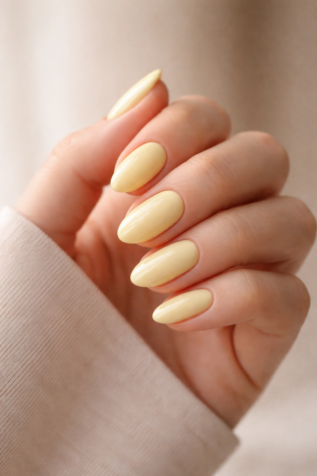 Close-up of short almond nails in soft yellow showing tapered edges