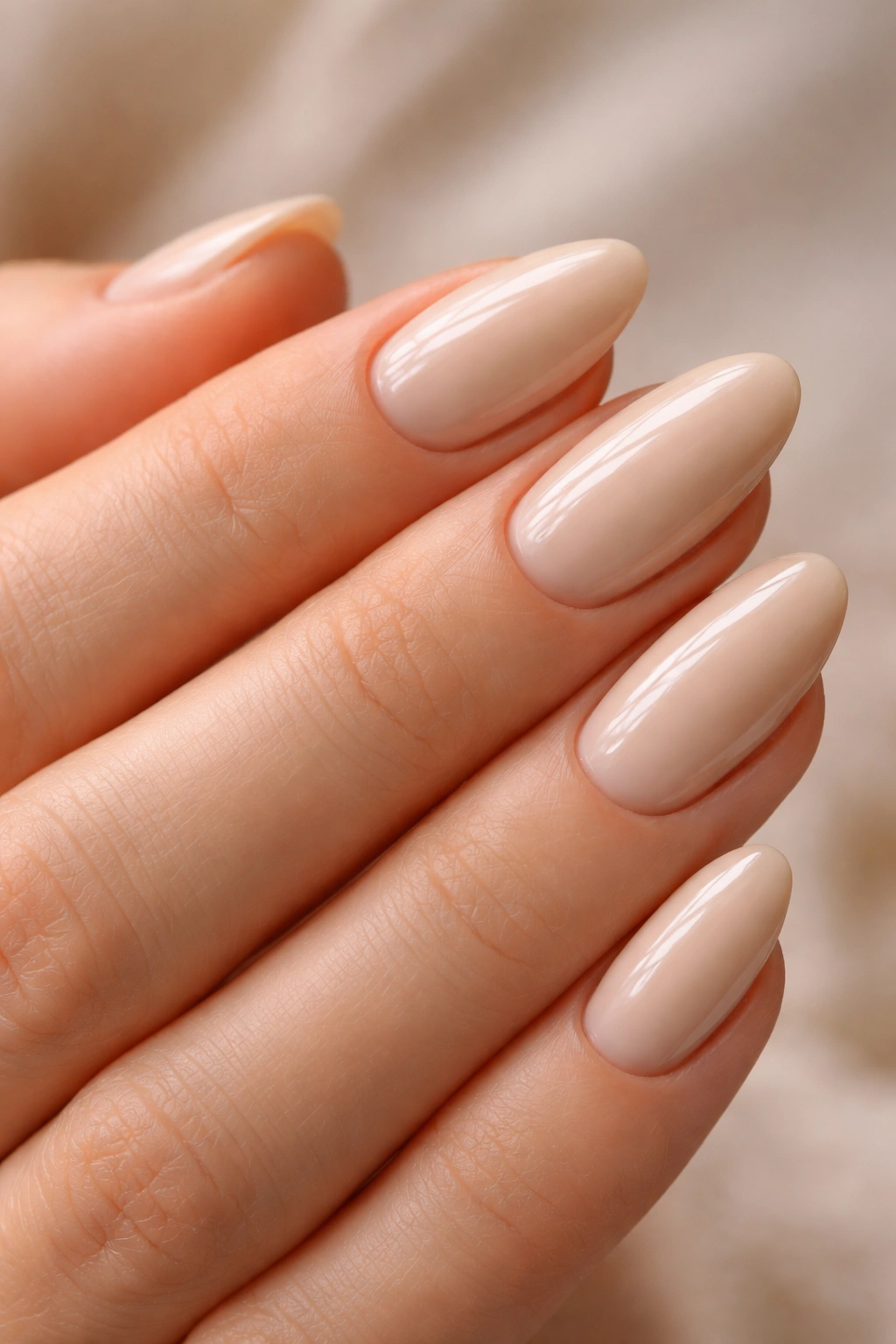 Close-up of short beige almond nails with a high-gloss finish