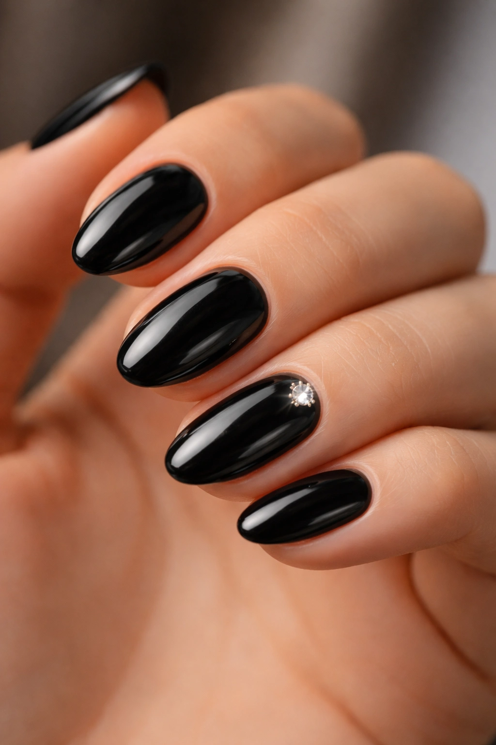 Close-up of short black almond nails with a single high-shine gem on one nail