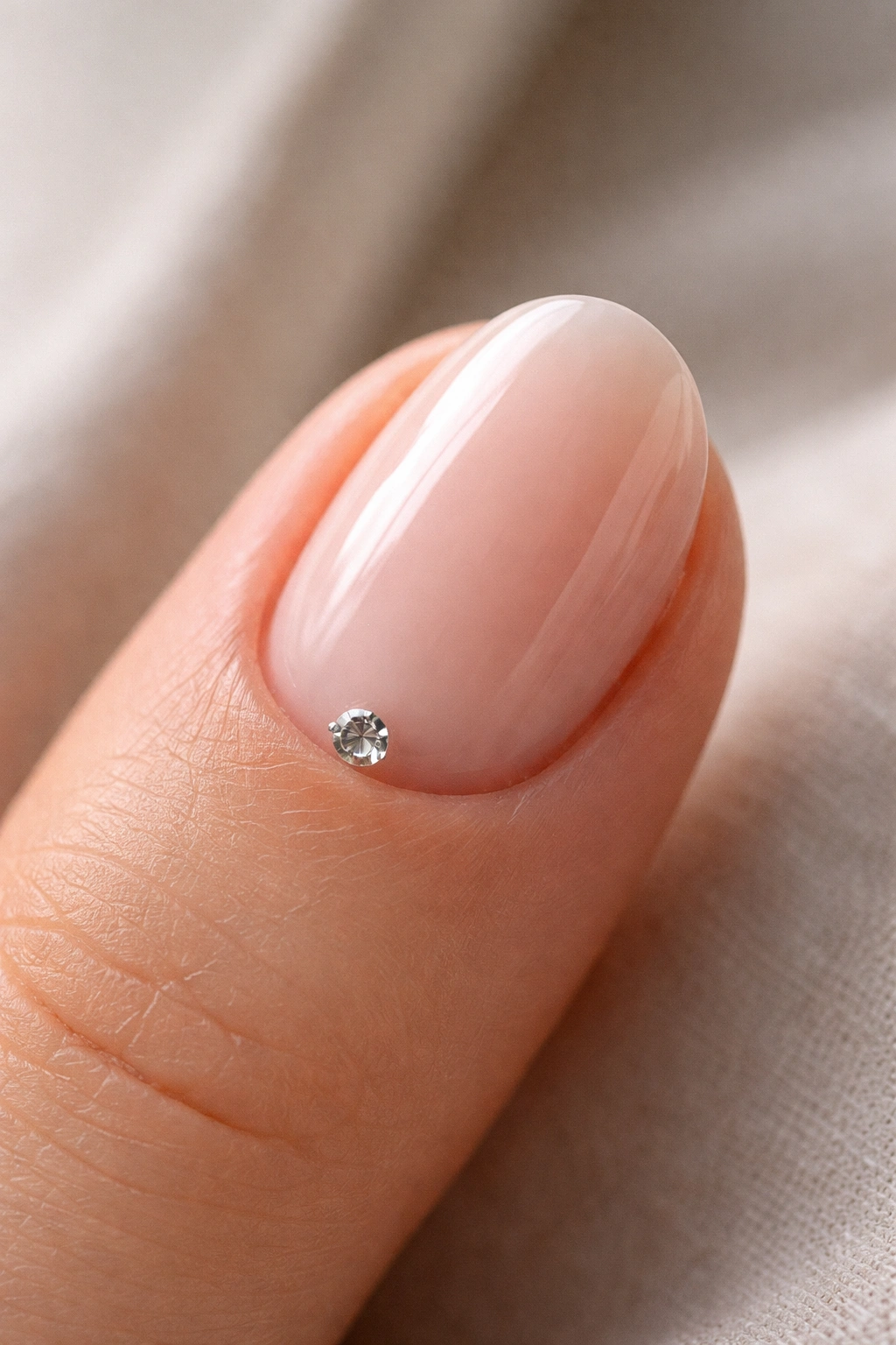 Close-up of a short oval nail with a single crystal at the cuticle on a milky pink nude base