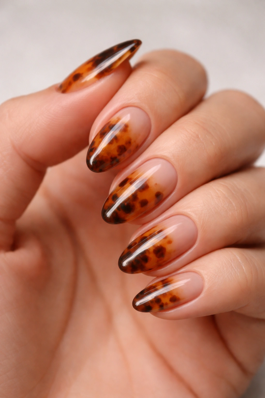 Close-up of short tortoiseshell almond nails with sheer nude base and amber-brown pattern, glossy finish