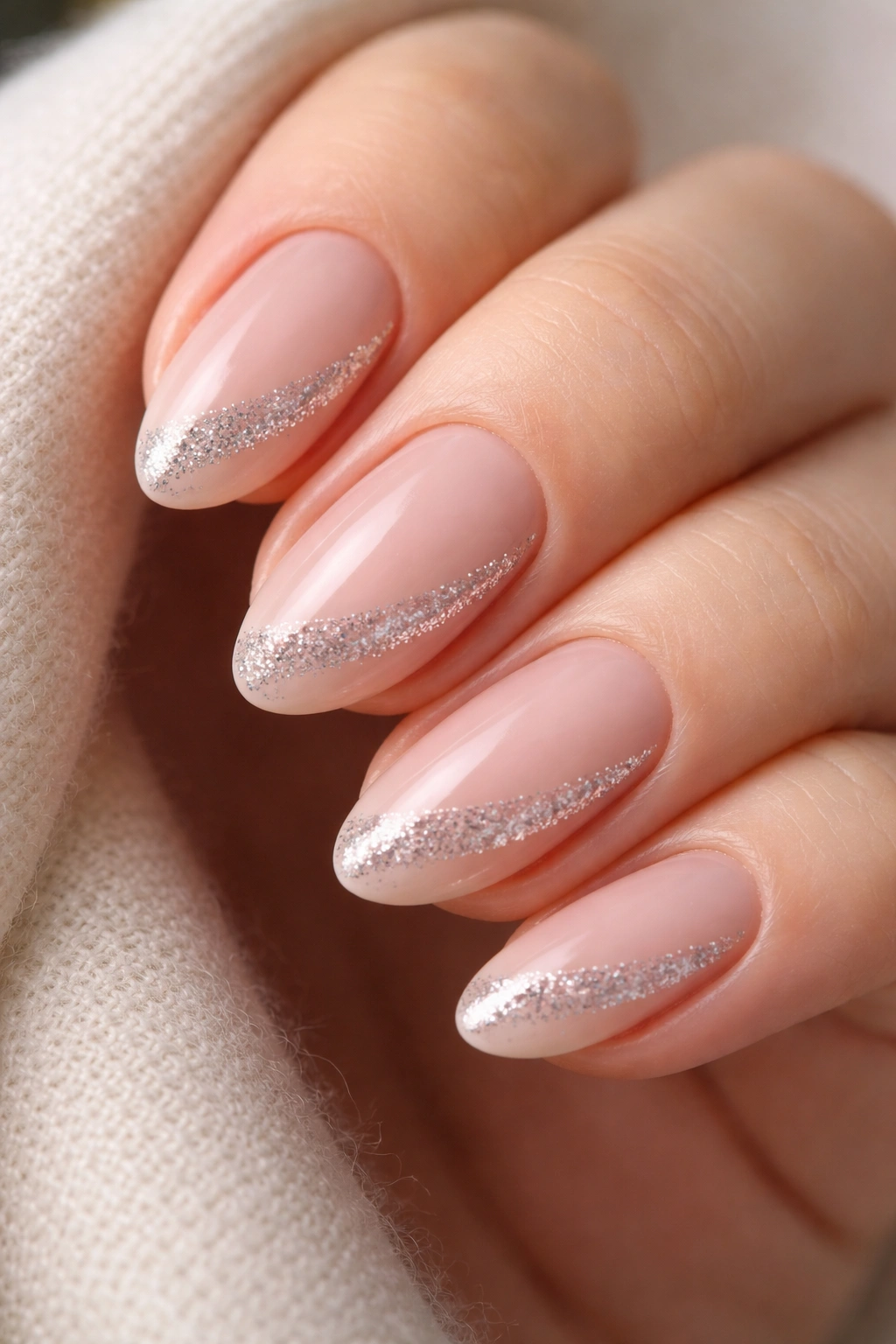 Close-up of short almond nails with diagonal glitter accent on a neutral background