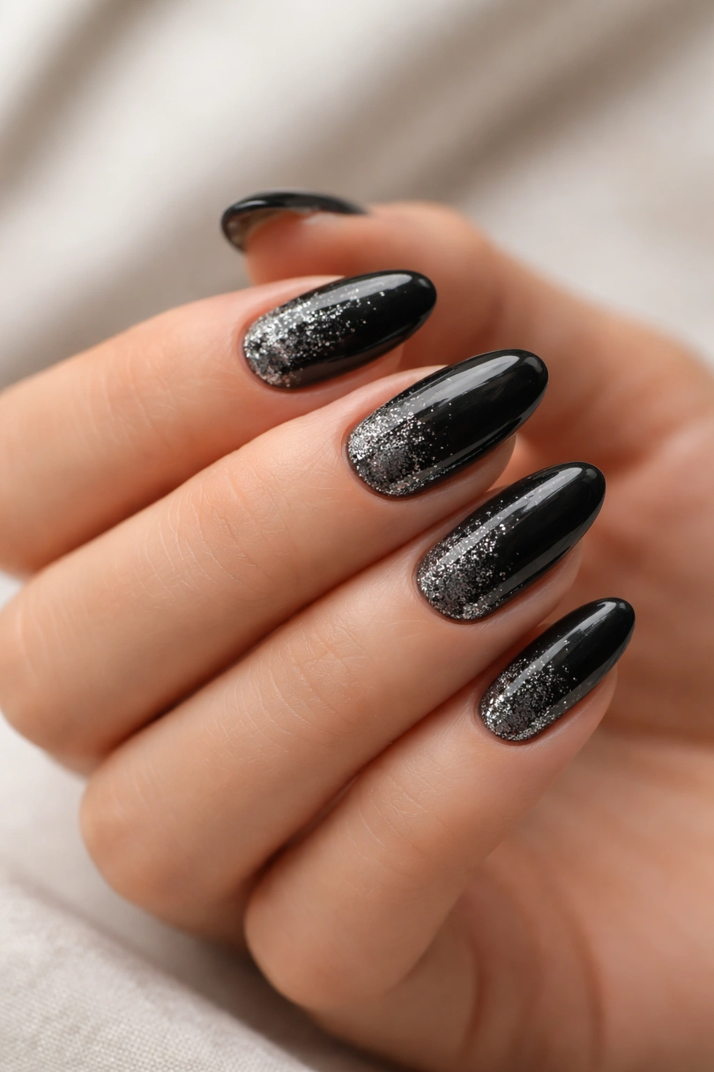 Close-up of short almond nails with diagonal side-swept black glitter.