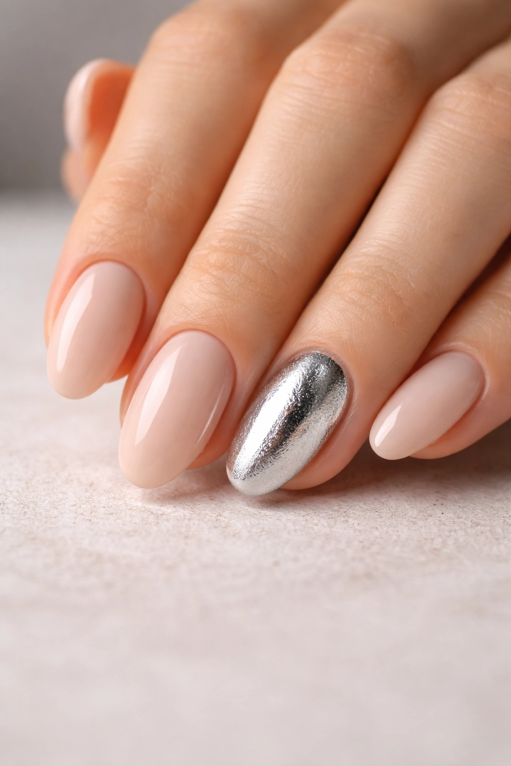 Close-up of a short almond manicure with a chunky silver accent nail on a neutral beige manicure