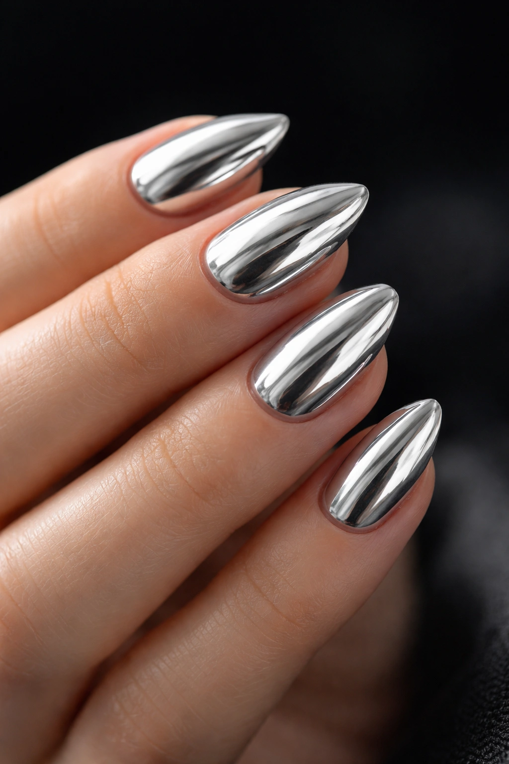 Close-up of silver mirror chrome almond nails on a hand with dark background