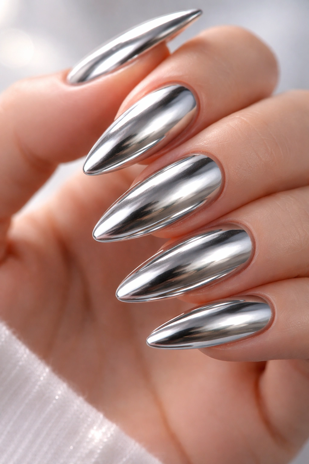Close-up of almond-shaped silver chrome nails on neutral background.