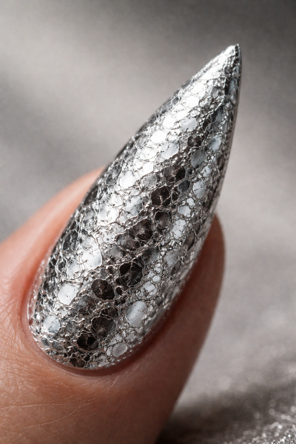 Close-up of a silver stiletto nail with foil texture reflecting light.