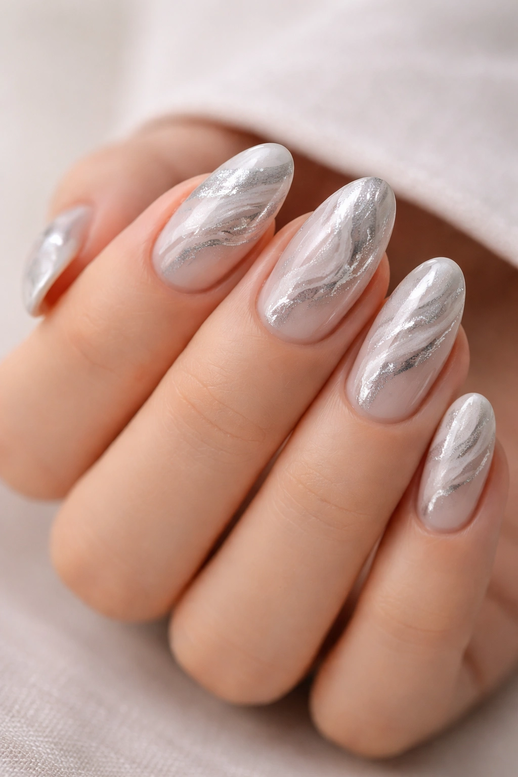 Close-up of short almond nails with silver marble pattern on a pale base