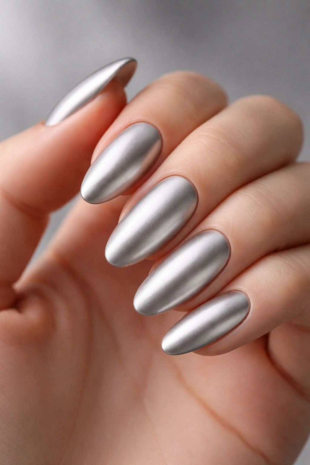 Close-up of almond nails with a classic silver matte chrome manicure in studio lighting
