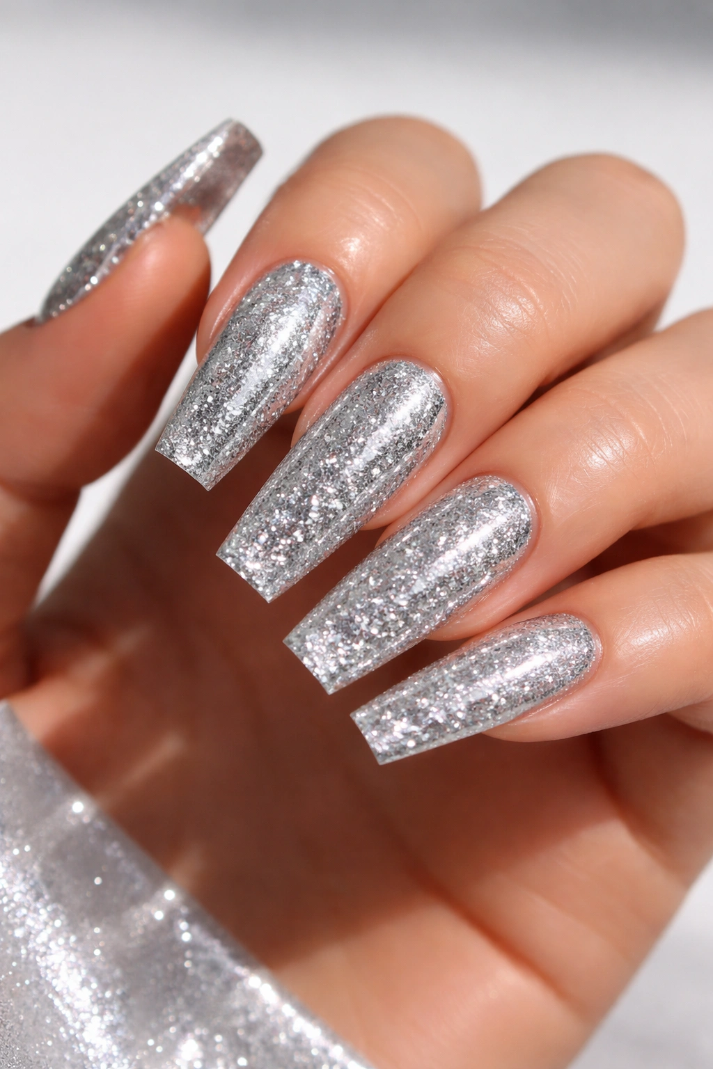 Close-up of coffin nail with highly reflective silver mirror glitter on a clear base.