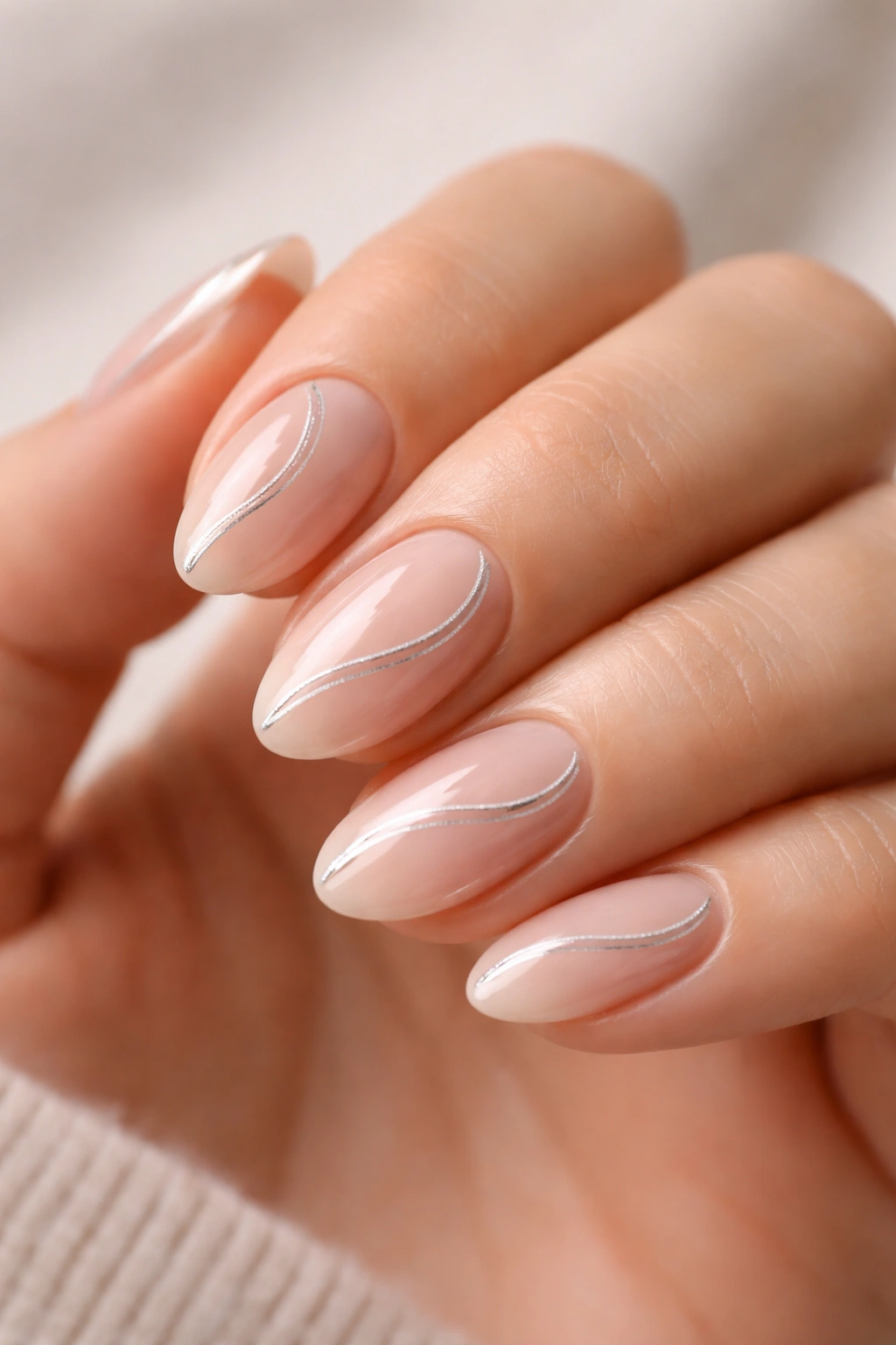 Close-up of short almond nails with a silver swirl on nude base