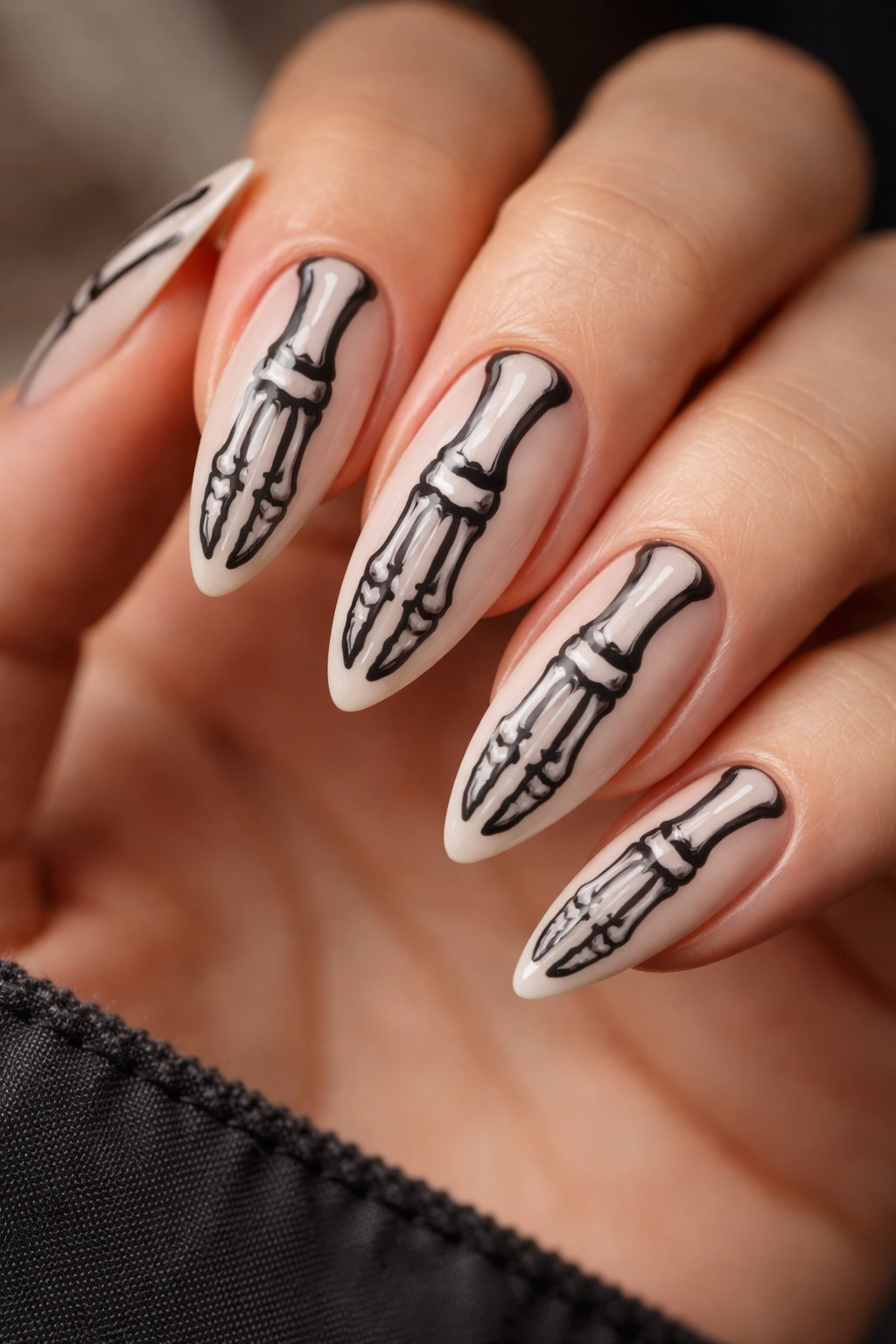 Almond nails with pale nude base and black bone lines resembling skeleton hand bones.