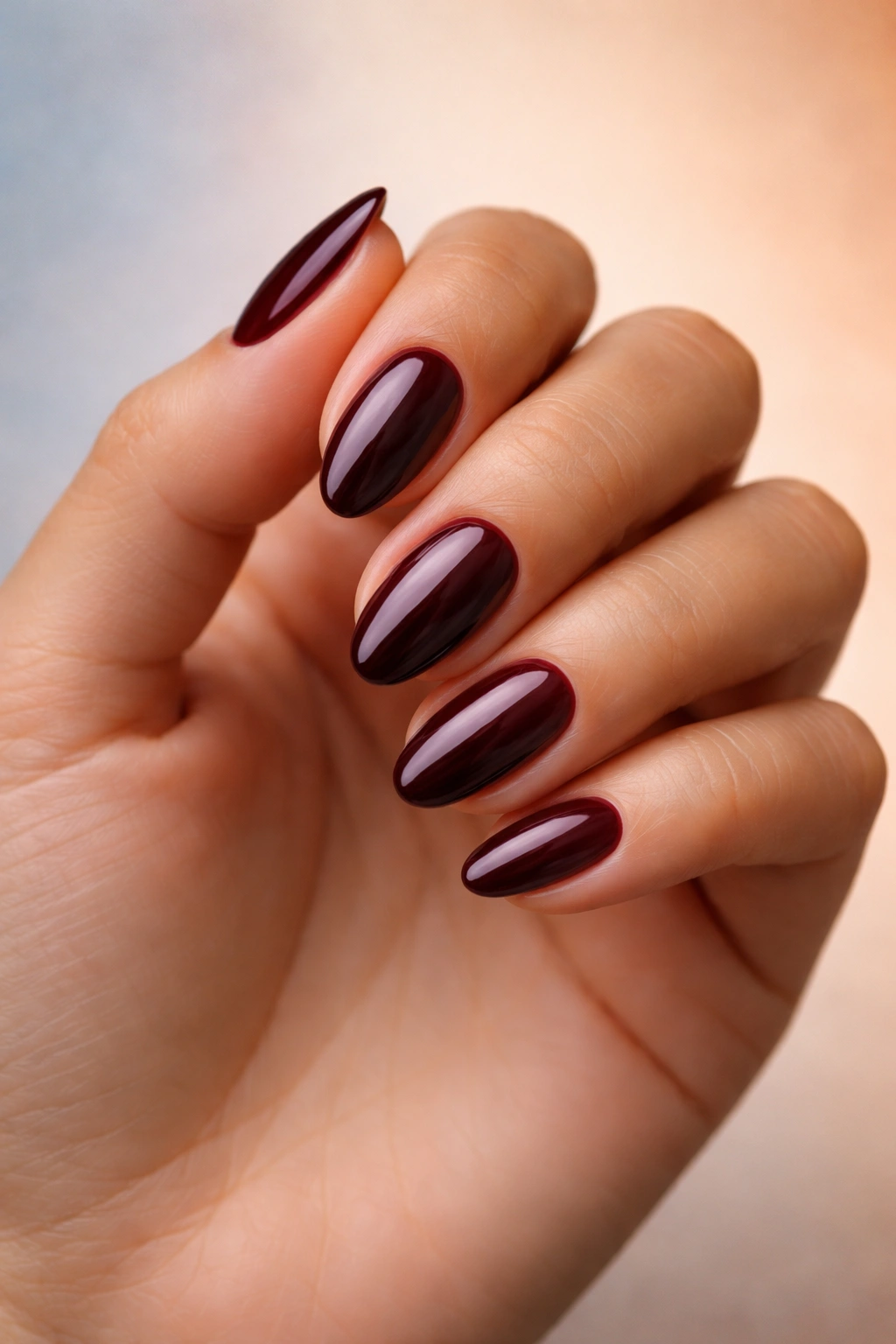 Close-up of burgundy almond nails on skin tone with gradient background