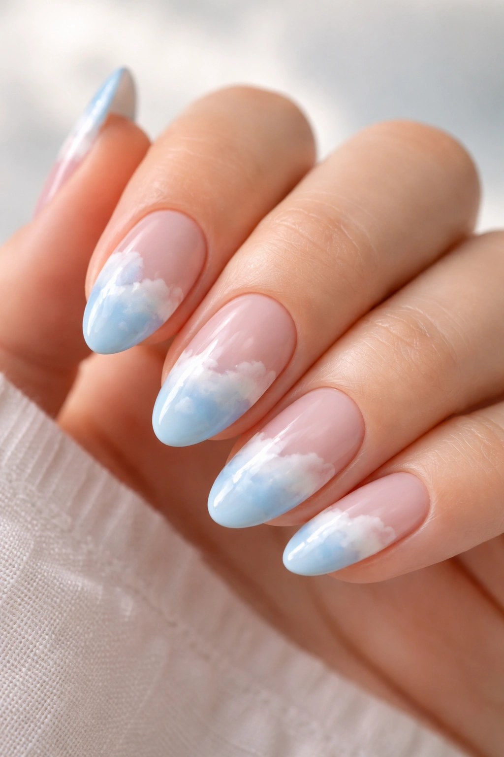 Close-up of short almond nails with sky blue base and white cloud tips
