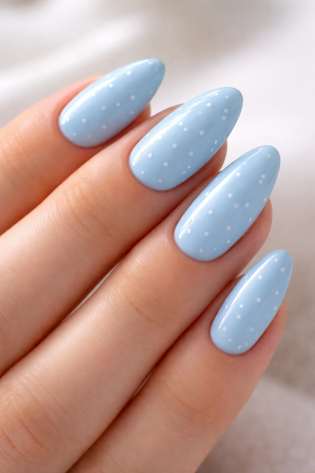 Close-up of sky blue almond nails with tiny white dots