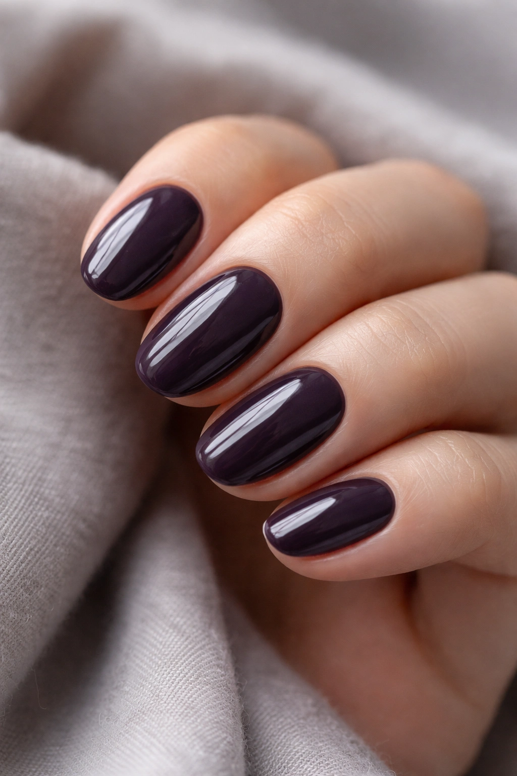 Close-up of smoky eggplant short oval nails with gray undertone and high-gloss finish