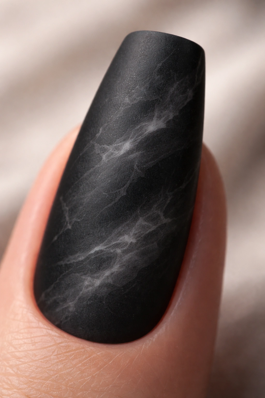 Close-up of a single matte black marble nail with smoky gray veining.