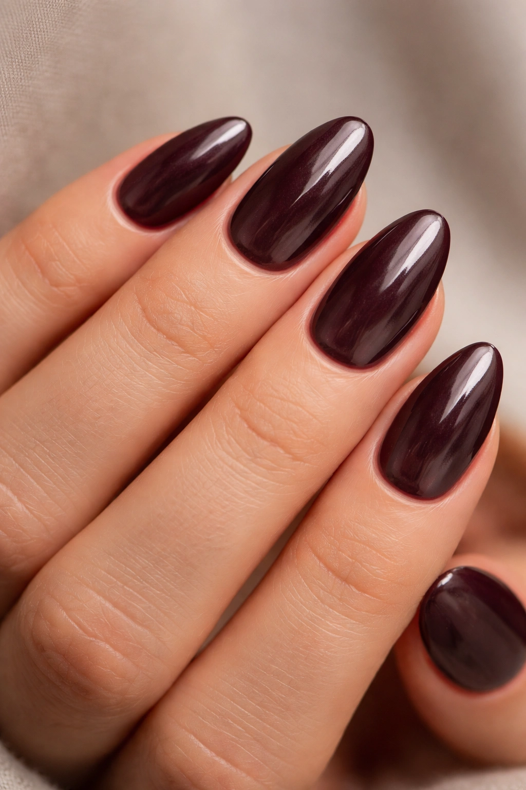 Close-up of short almond nails in smoky merlot shade with glassy finish