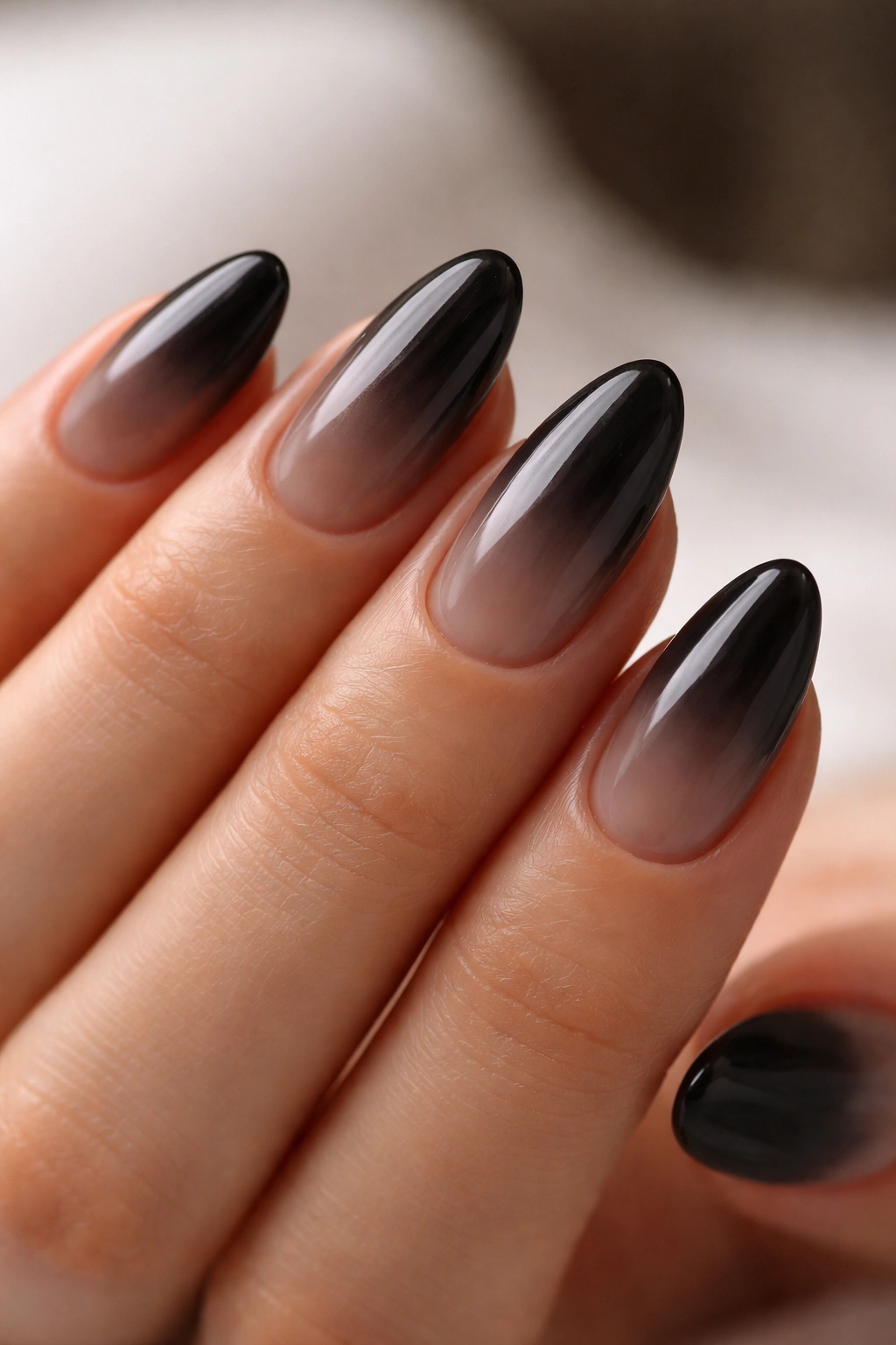 Close-up of smoky black almond nails with sheer overlay on a neutral background