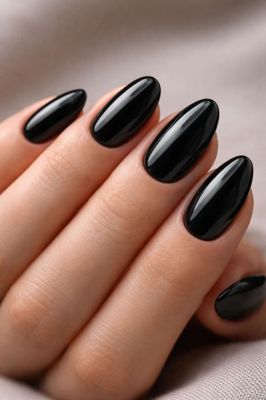 Close-up of short almond nails with glossy black polish on a bare hand