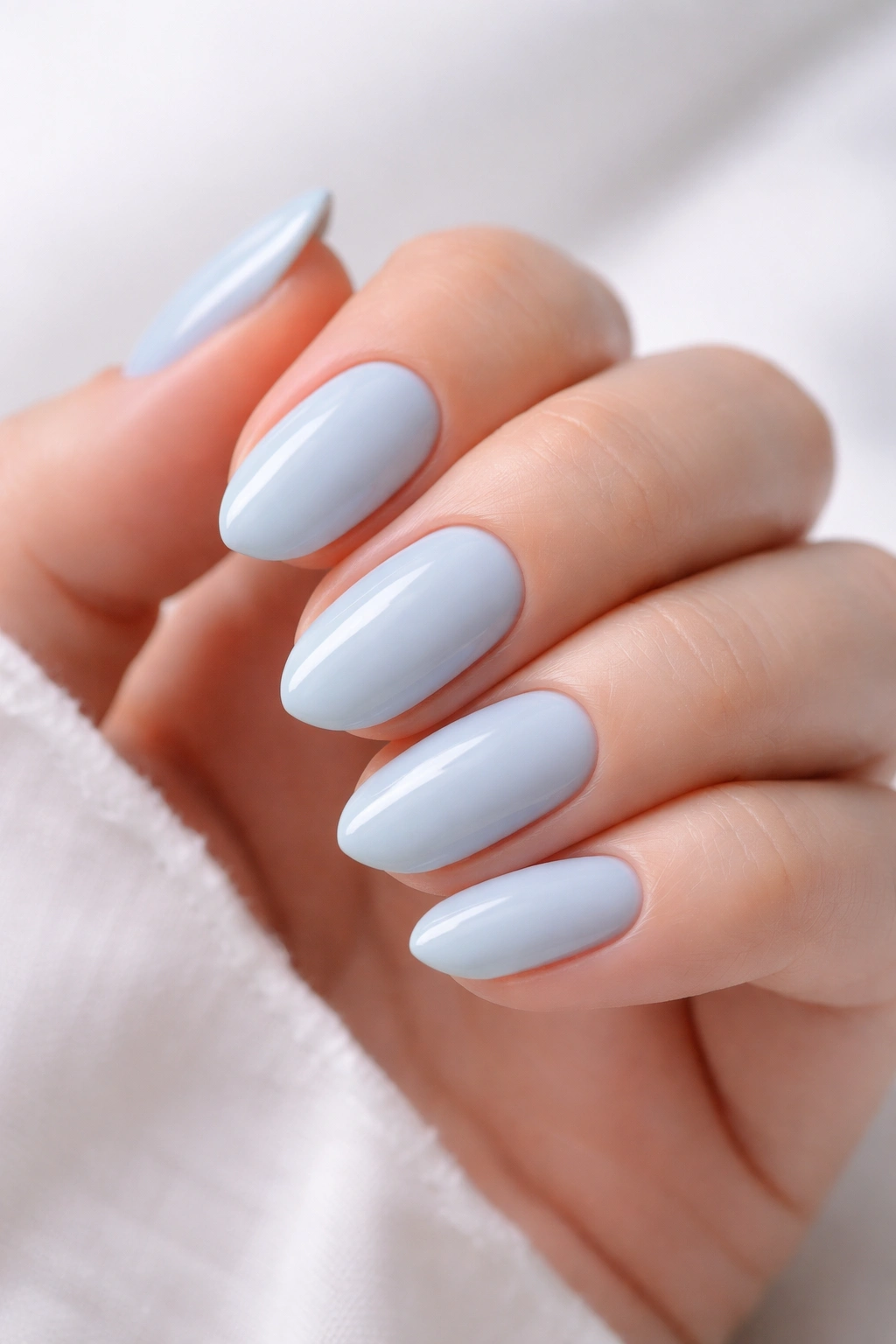 Close-up of short almond nails painted soft baby blue with a milky finish