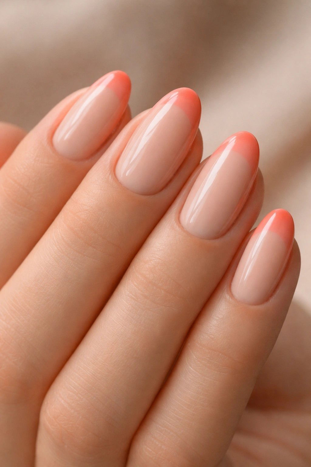 Close-up of a short almond nail with soft coral tip on warm beige base