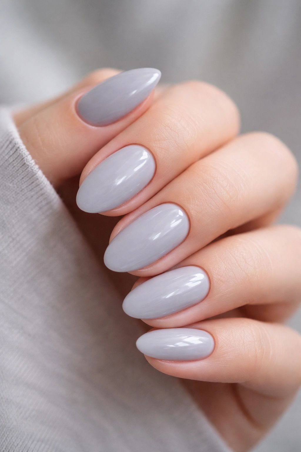 Close-up of short almond nails painted soft gray with a subtle blue-lavender tint and a glossy finish