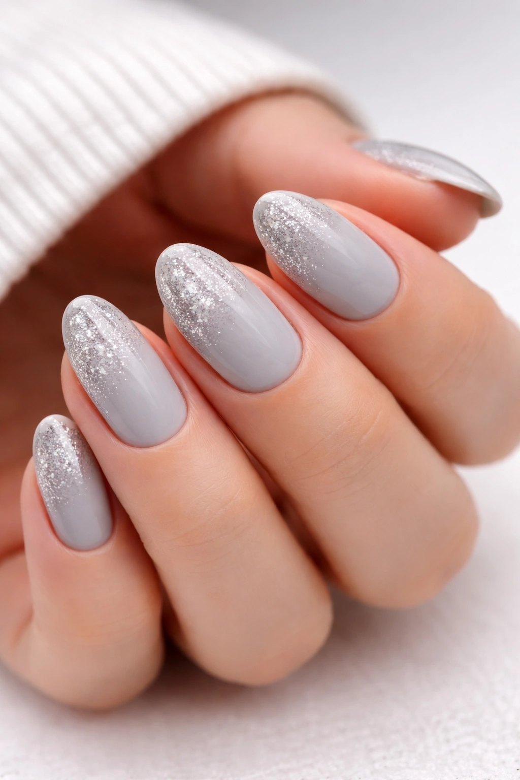 Close-up of short almond nails with soft gray base and silver glitter fade