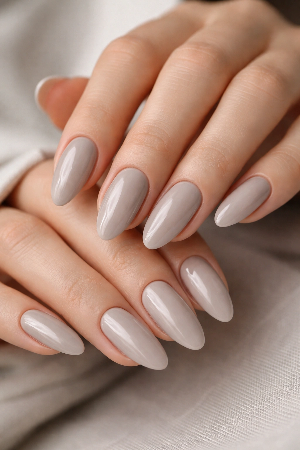 Close-up of hands with soft gray nude tapered oval nails on a neutral background