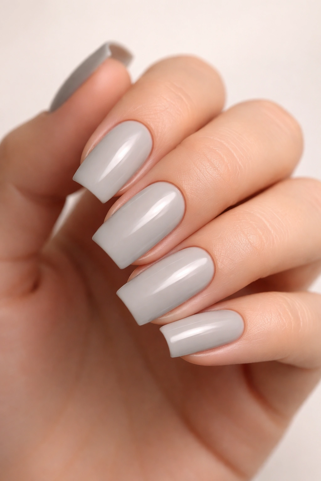 Close-up of a hand with soft warm gray squoval nails on a neutral studio backdrop