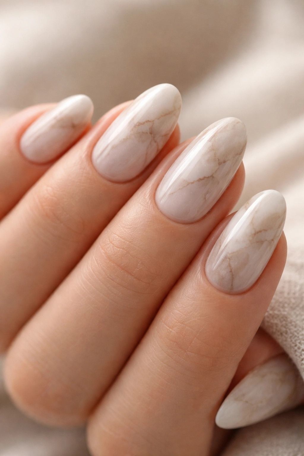 Close-up of soft neutral-toned marble nails on almond shapes with subtle veining