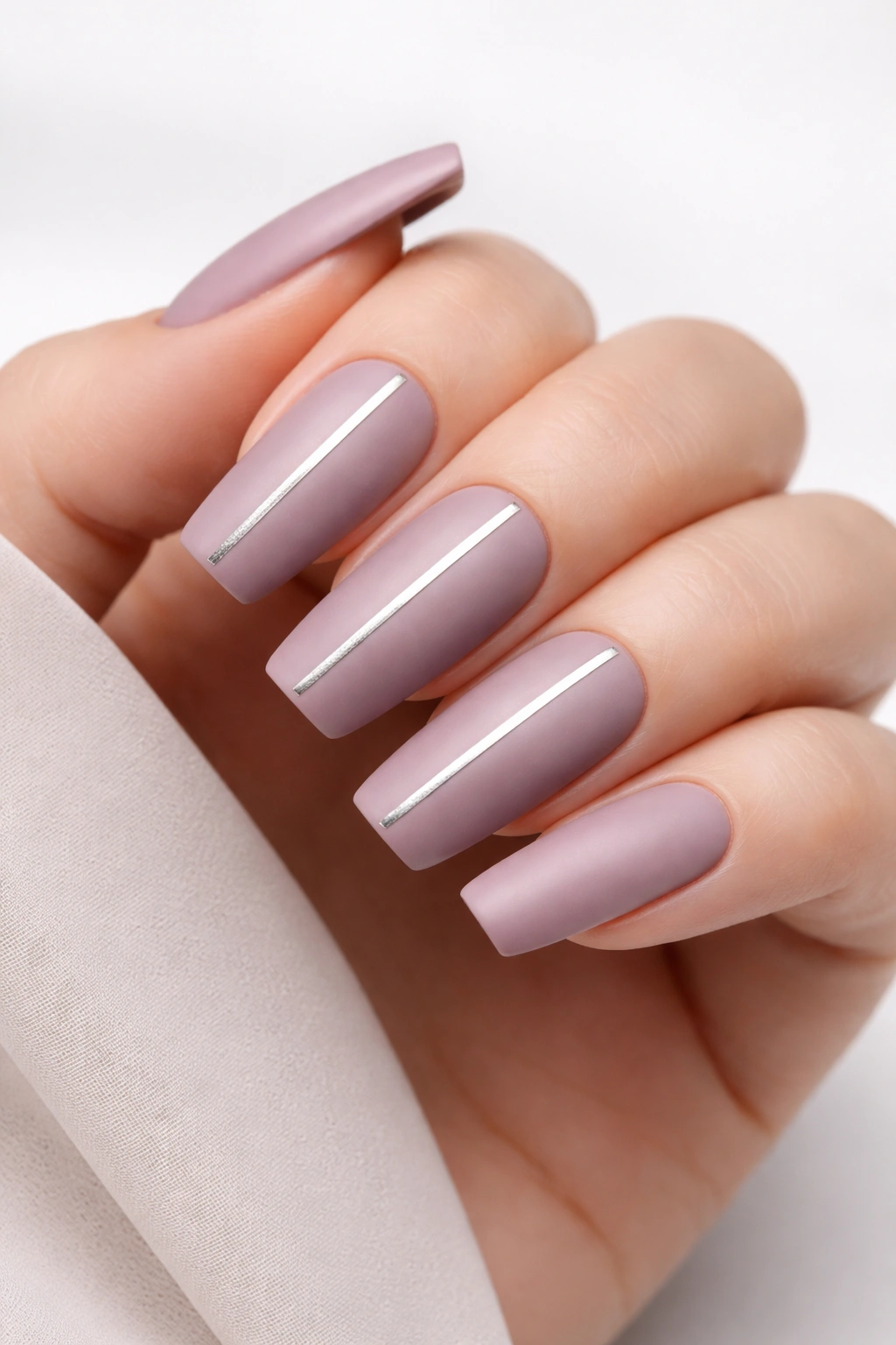 Close-up of long squoval nails with soft mauve matte polish, silver stripes, and a plain matte accent nail
