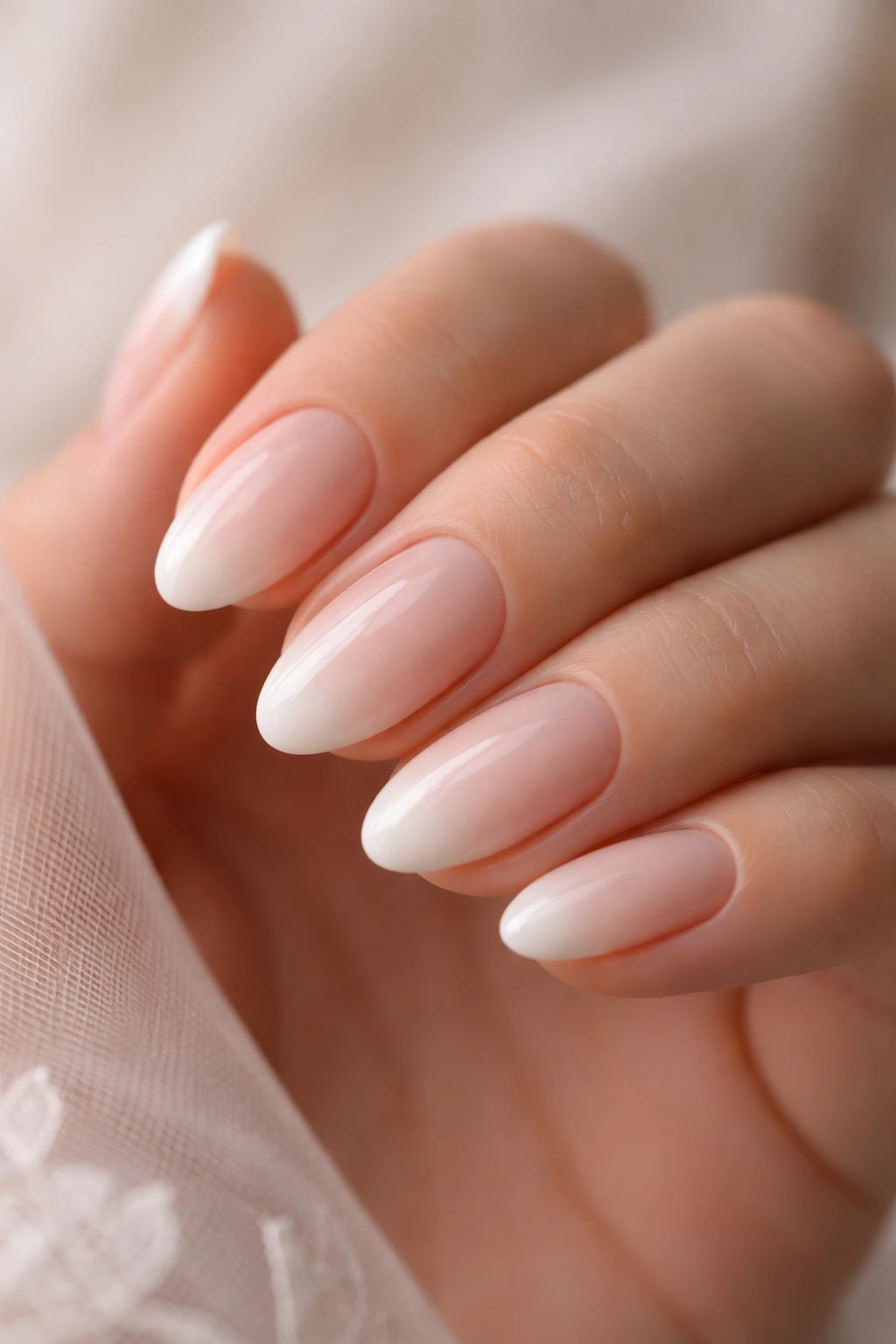 Close-up of short almond nails with soft milky tips on a neutral background