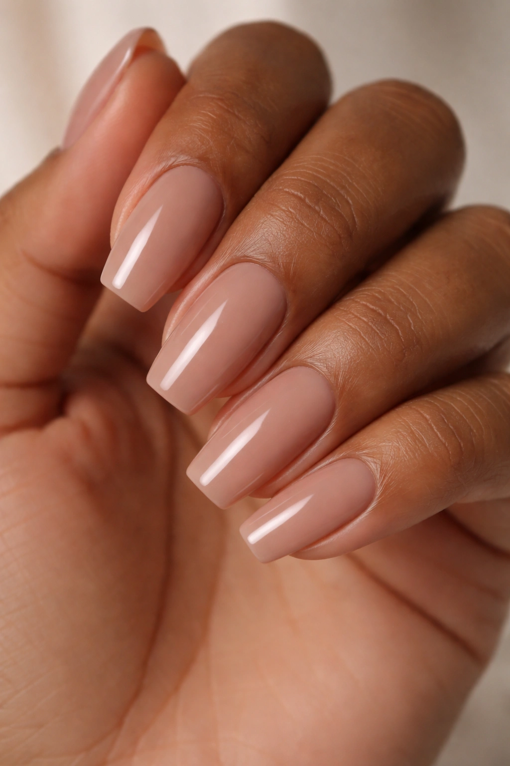 Close-up of hand with soft mocha nude nails on a short ballerina tip.