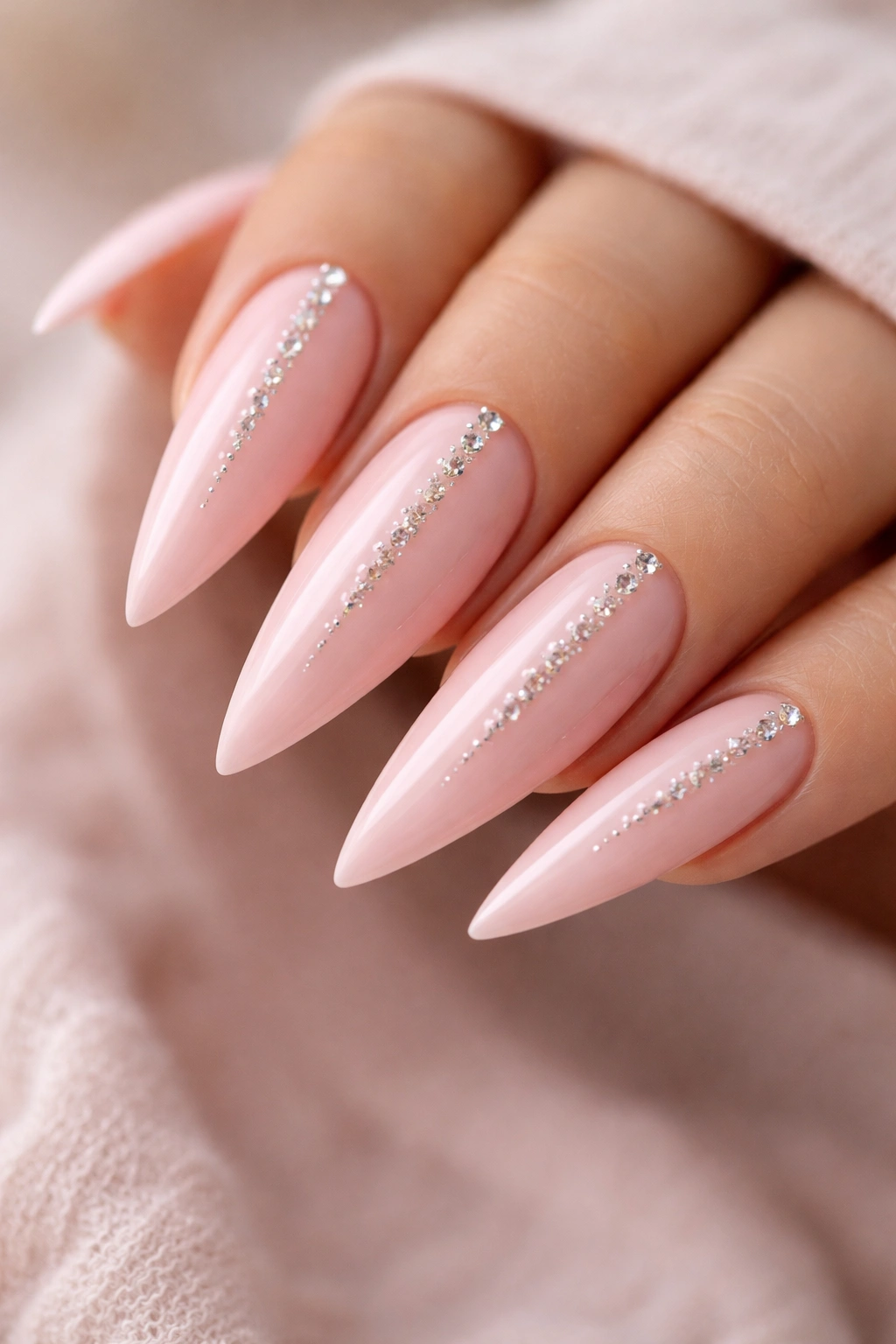 Close-up soft pink stiletto nails with micro diamonds along the center line.