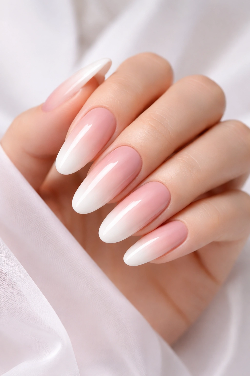 Close-up of long oval nails in a soft pink to white ombre with a glossy finish