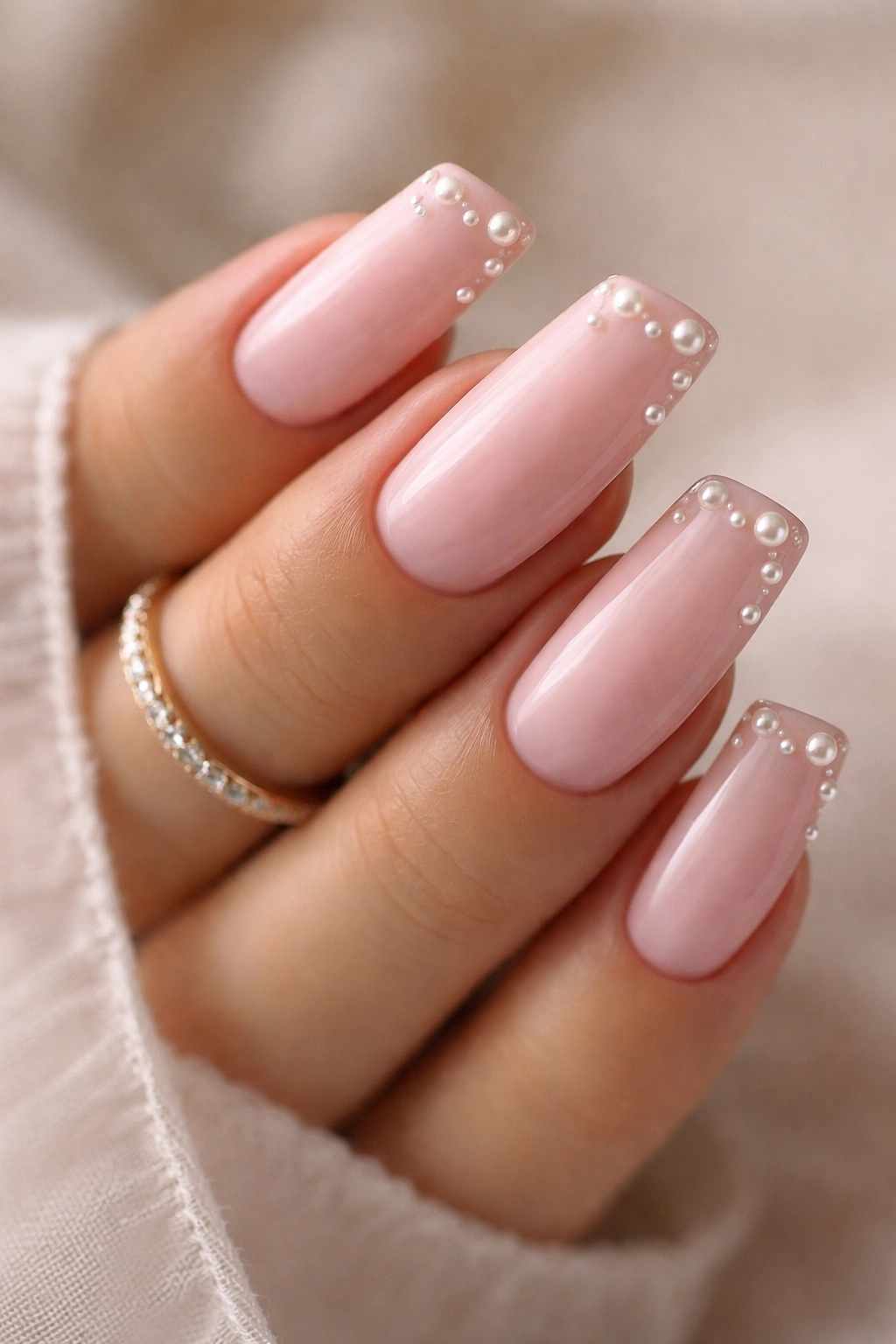 Close-up of soft pink duck nails with pearl accents on tips
